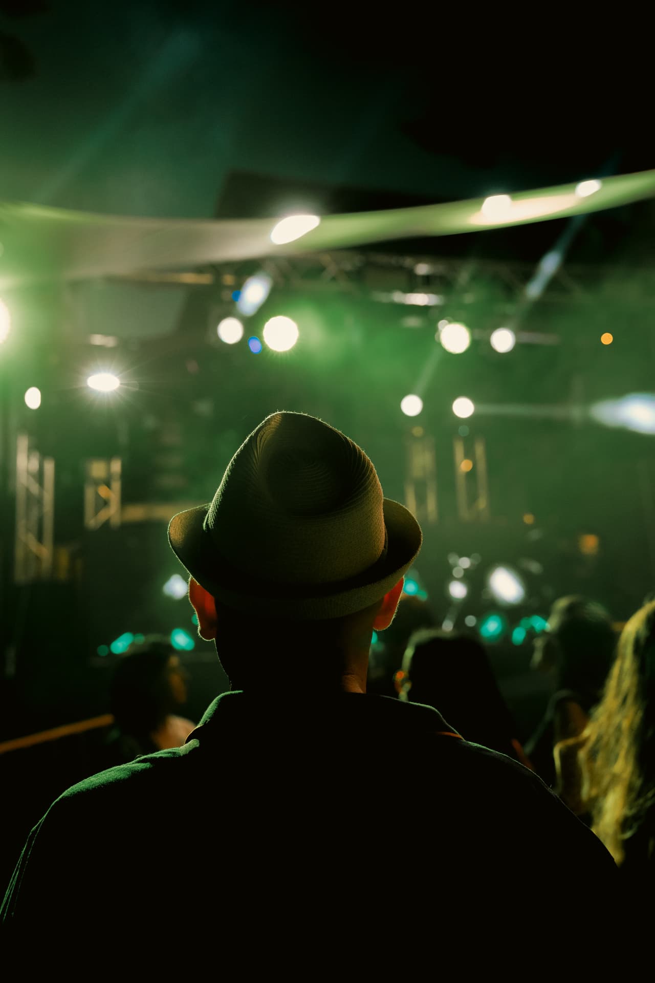 Guest in a hat facing the green-lit stage